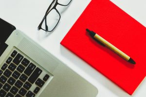 keyboard, notepad, pen, and glasses on a desk as we write poetry on PowerPoint for Publication
