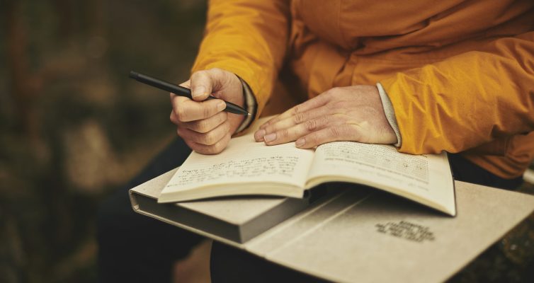 the hands of an adult writing on a journal with mindfulness writing techniques. Image by Pexels